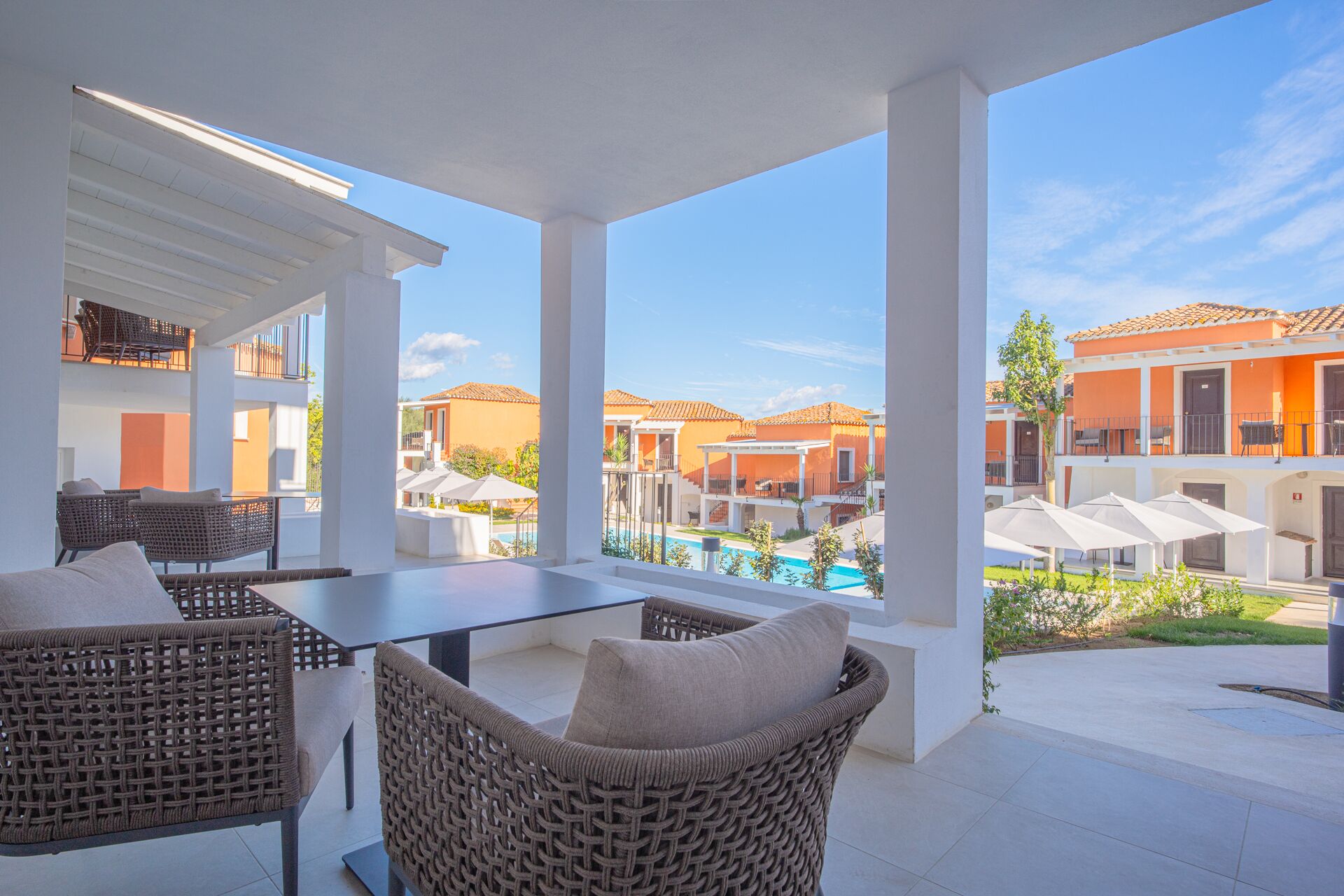 A covered outdoor area with wicker furniture and a view of a pool and buildings.