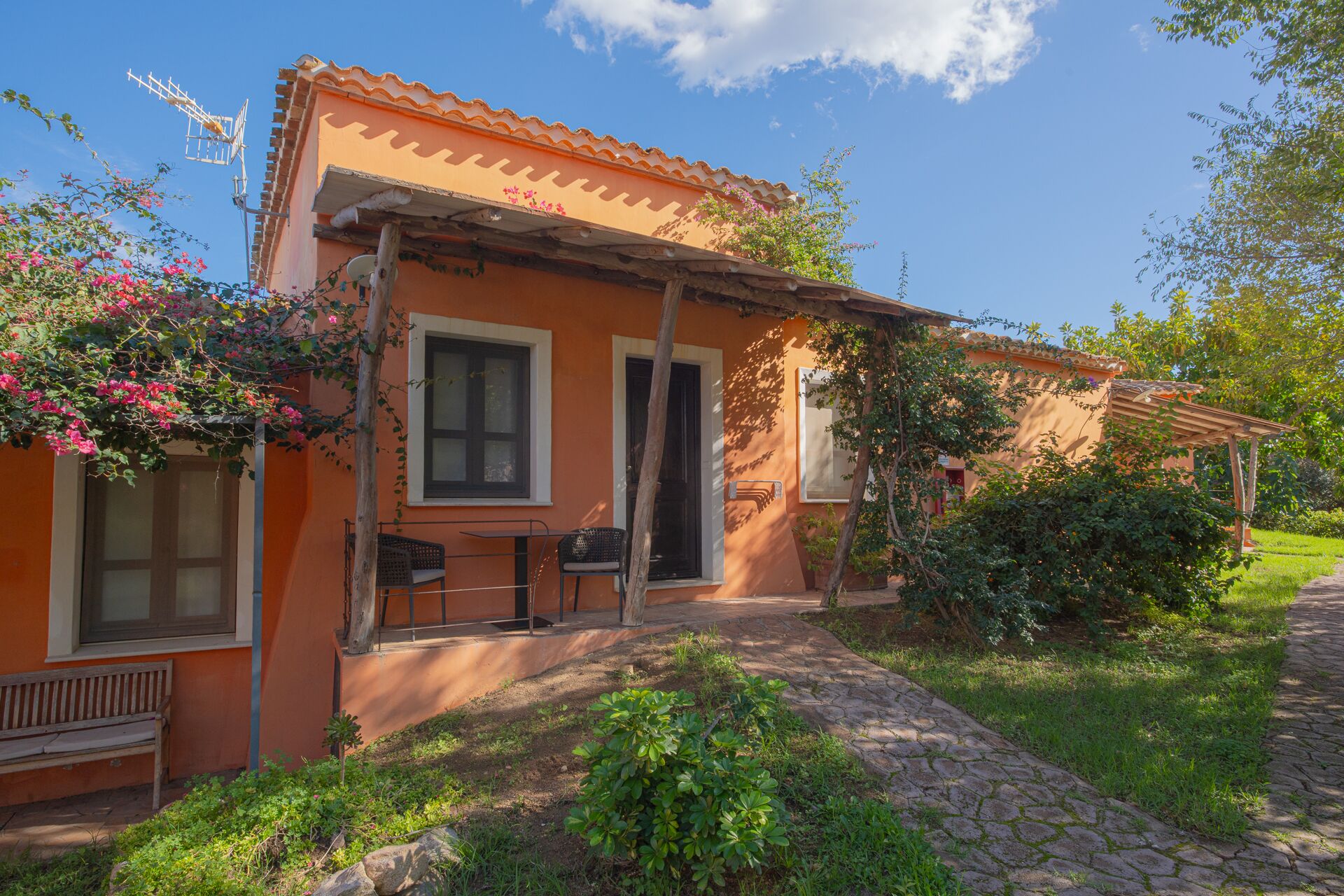 A house with a tiled roof, a porch with a bench, and a stone pathway leading to the entrance.