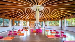 Amplia habitación con techo alto y ventanas grandes, con colchonetas y bloques de yoga dispuestos para una clase.