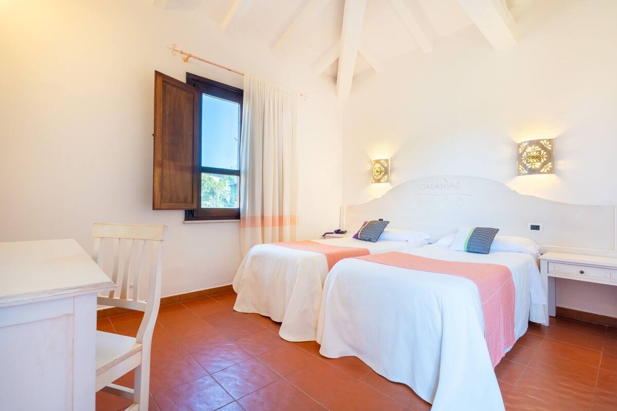 Un dormitorio con dos camas, una ventana con cortinas, un escritorio y una silla.