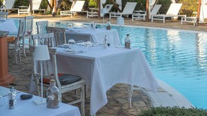 Zona de comedor al aire libre con mesas dispuestas para una comida, con vistas a una piscina.