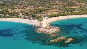Vista aérea de un pueblo costero con playa, aguas turquesas cristalinas y un promontorio rocoso en el centro.