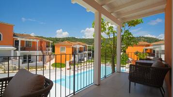 Ein überdachter Balkon mit Korbmöbeln, ein Pool und im Hintergrund orangefarbene Gebäude.