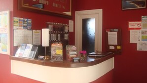 A reception desk with a red wall, various informational posters, a window, and a door. - Hotel Costa Cántabra (Argonos)