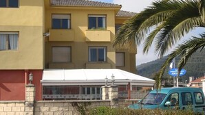 A yellow building with a white awning, a stone wall, and a parked turquoise car. - Hotel Costa Cántabra (Argonos)