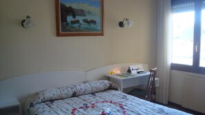 A bedroom with a bed, a nightstand, a painting, and a window. - Hotel Costa Cántabra (Argonos)