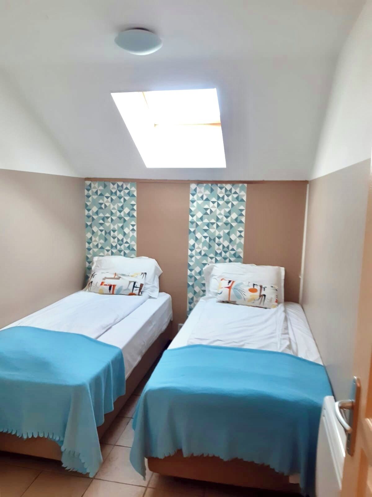 Una habitación pequeña con dos camas individuales, un tragaluz y papel tapiz estampado.