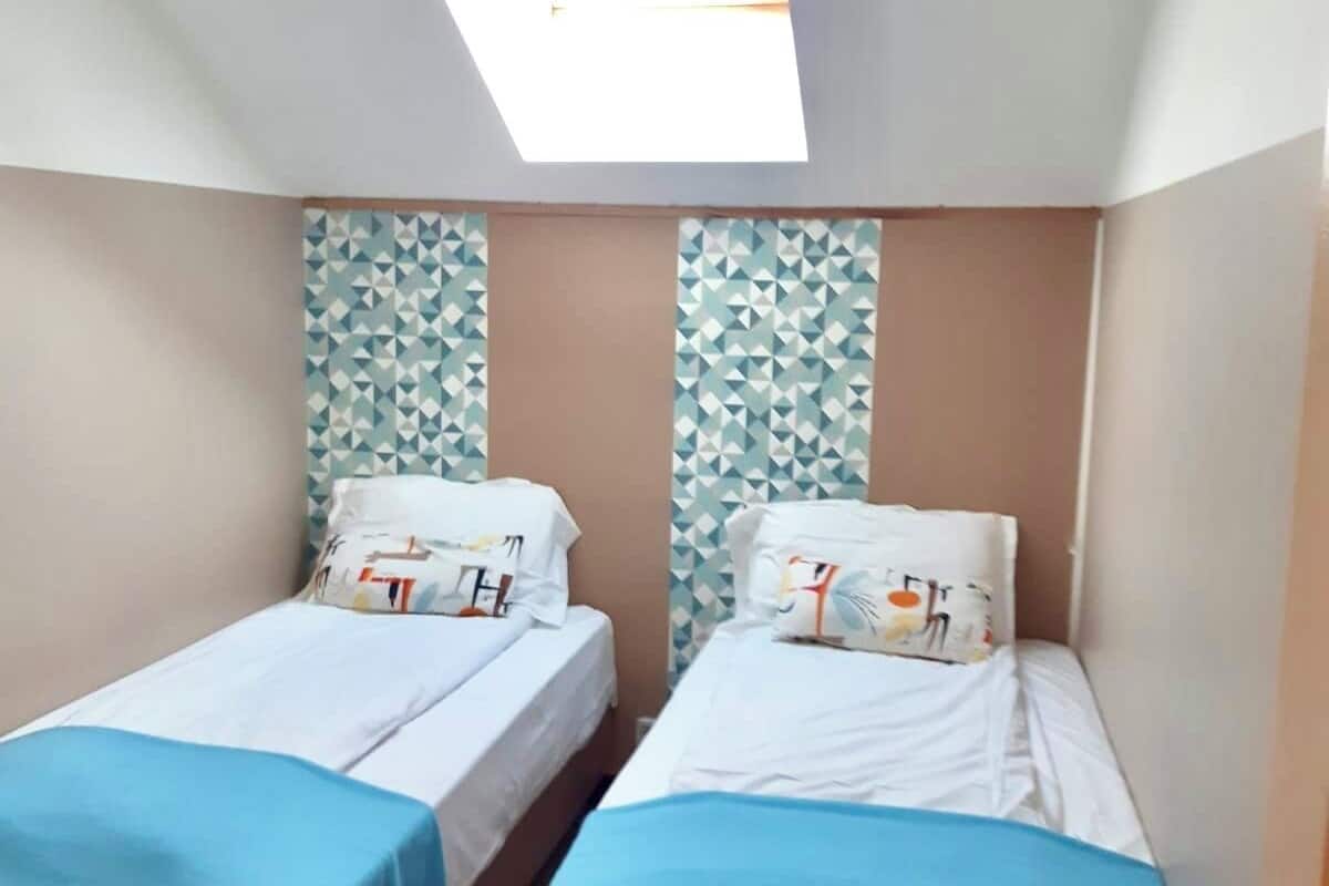A small room with two single beds, a skylight, and patterned wallpaper.