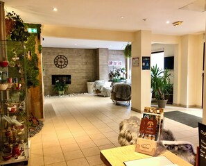 A hotel lobby with a fireplace, a clock, and a reception desk. - Adonis Valberg (Guillaumes)