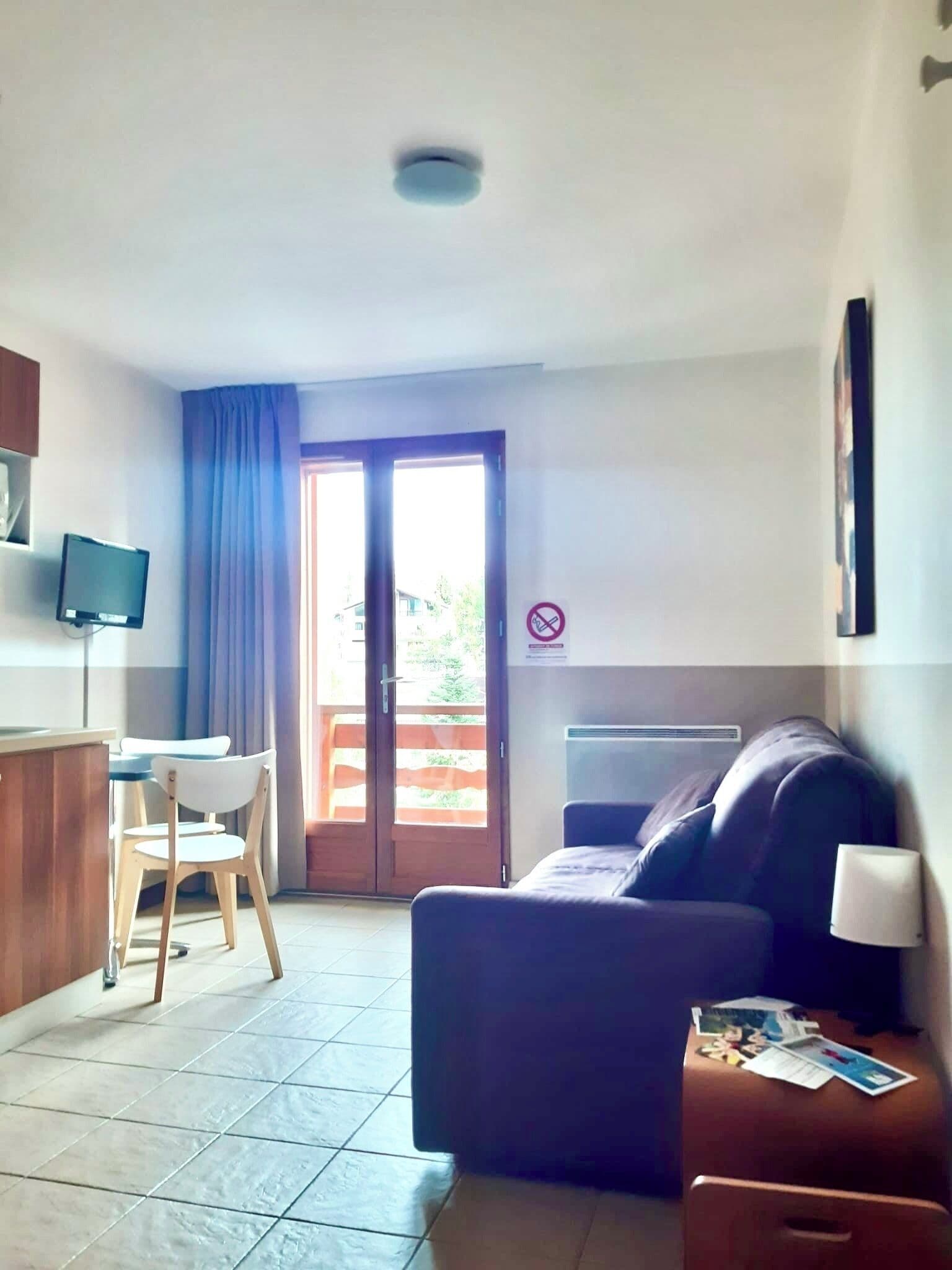 A compact living space with a sofa, a small table, a chair, a television, and a sliding glass door leading to an outdoor area.