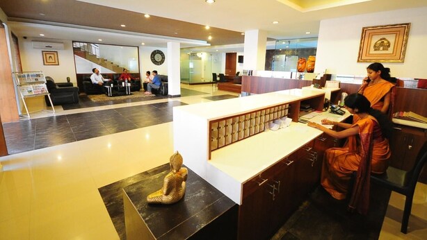 A hotel lobby with a reception desk, seating area, and a staircase leading to upper floors. - The Viceroy Comforts (Mysore)