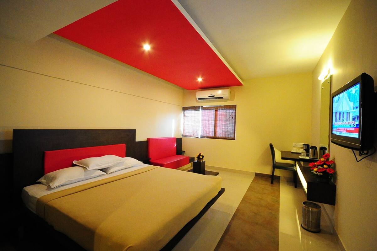 Une chambre d’hôtel avec un lit, un mur d’accent rouge, une télévision, un bureau et une fenêtre avec des stores.