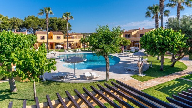 A swimming pool surrounded by lounge chairs and palm trees, with buildings in the background.