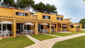 A yellow building with outdoor seating areas, each with white chairs and umbrellas.
