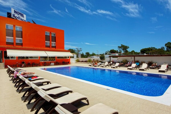 A hotel with a swimming pool, sun loungers, and a red building facade. - Hotel Zodiaco (Loulé)