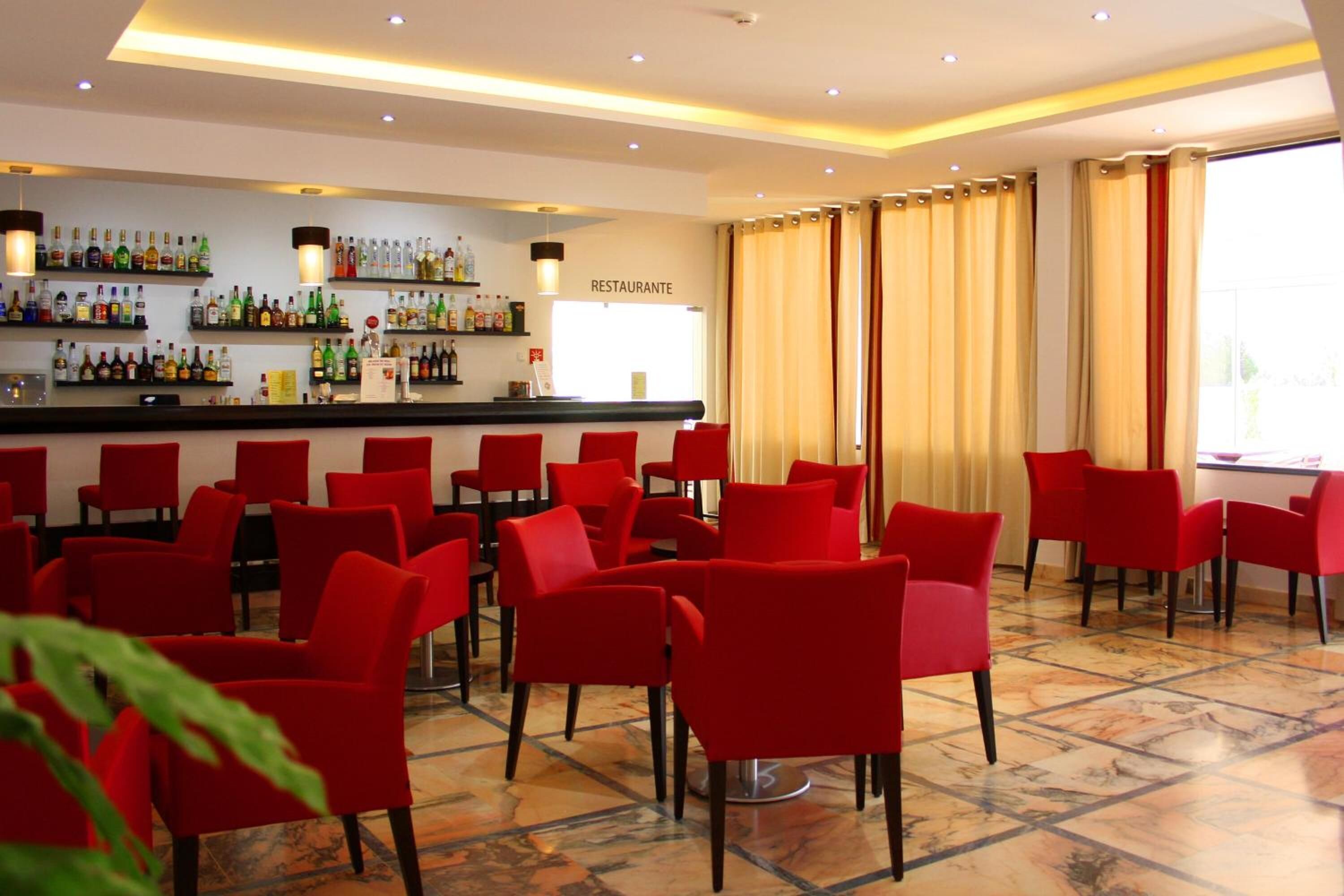 Un restaurant avec des chaises rouges et un coin bar où sont exposées différentes bouteilles.