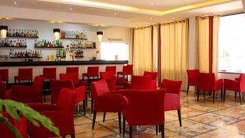 Un restaurant avec des chaises rouges et un coin bar où sont exposées différentes bouteilles.
