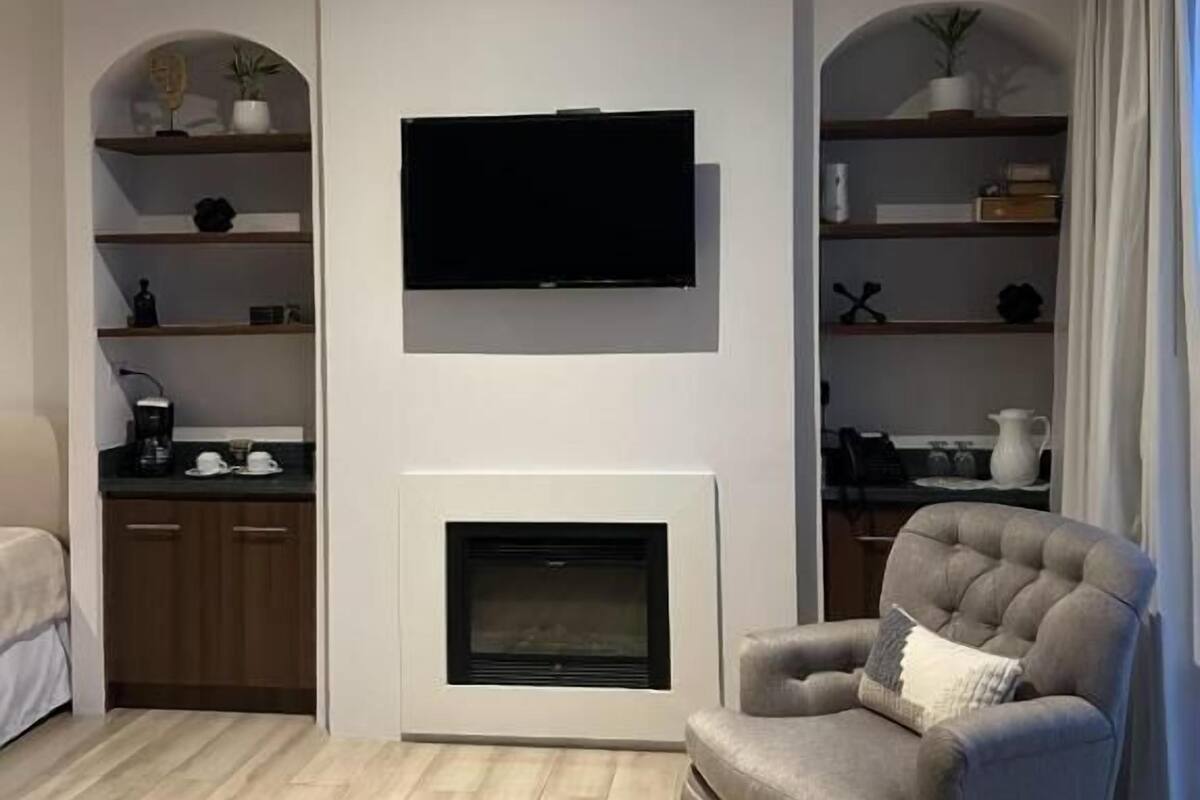 Una sala de estar moderna con un televisor de pantalla plana sobre una chimenea, piso de madera y estanterías empotradas con objetos decorativos.