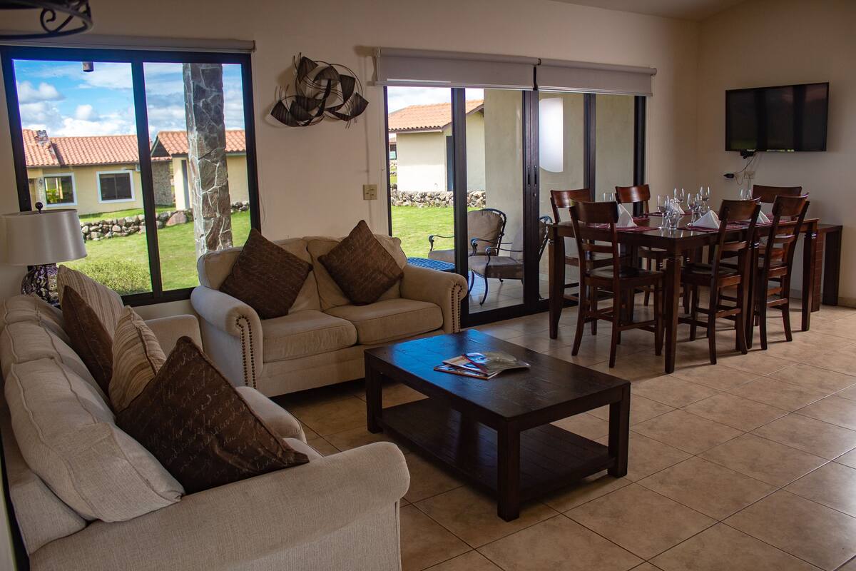 Una sala de estar con un sofá, una mesa de centro y un comedor con sillas y una mesa dispuesta para una comida.