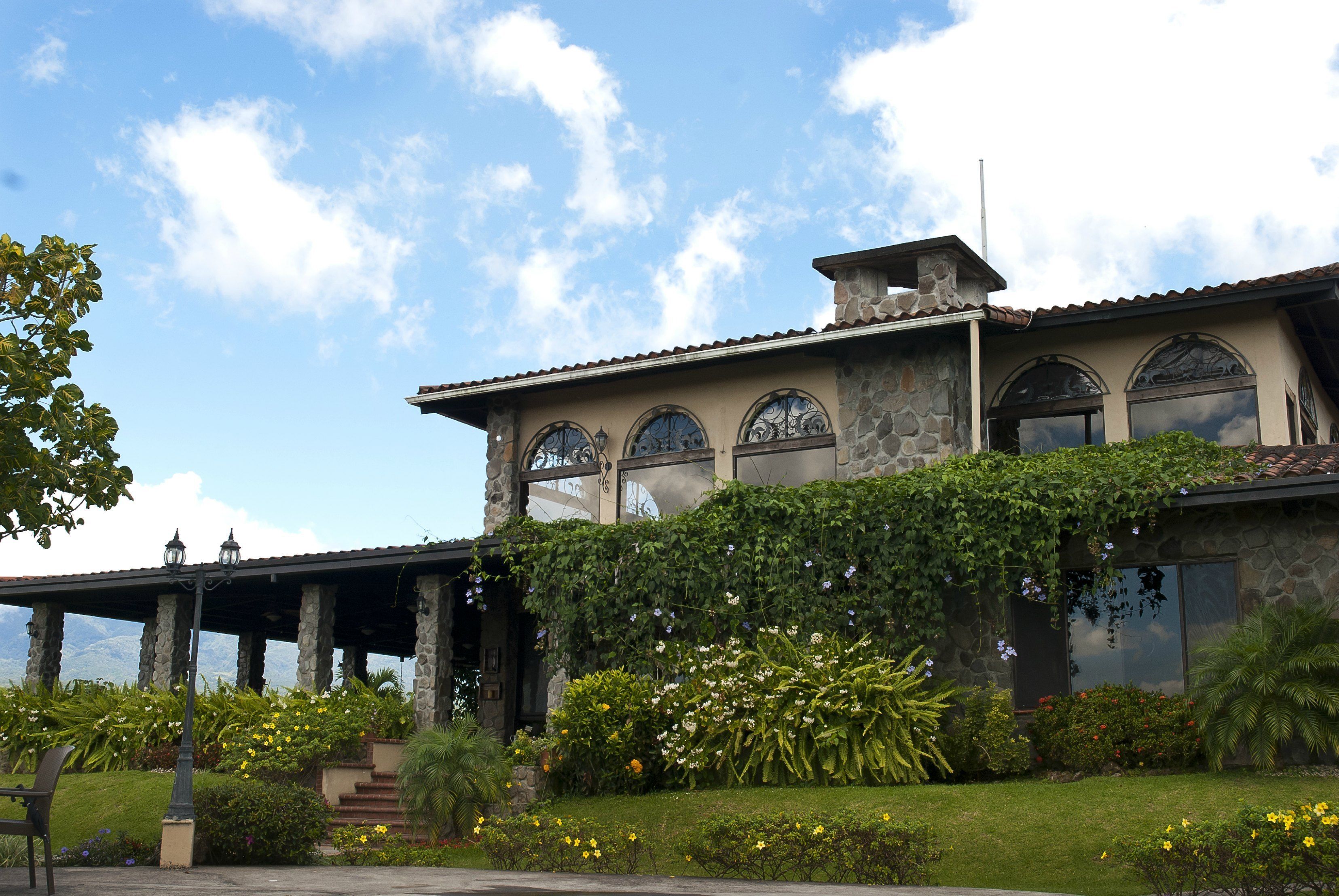 Un edificio de piedra con ventanas arqueadas, un patio cubierto y un jardín bien cuidado.