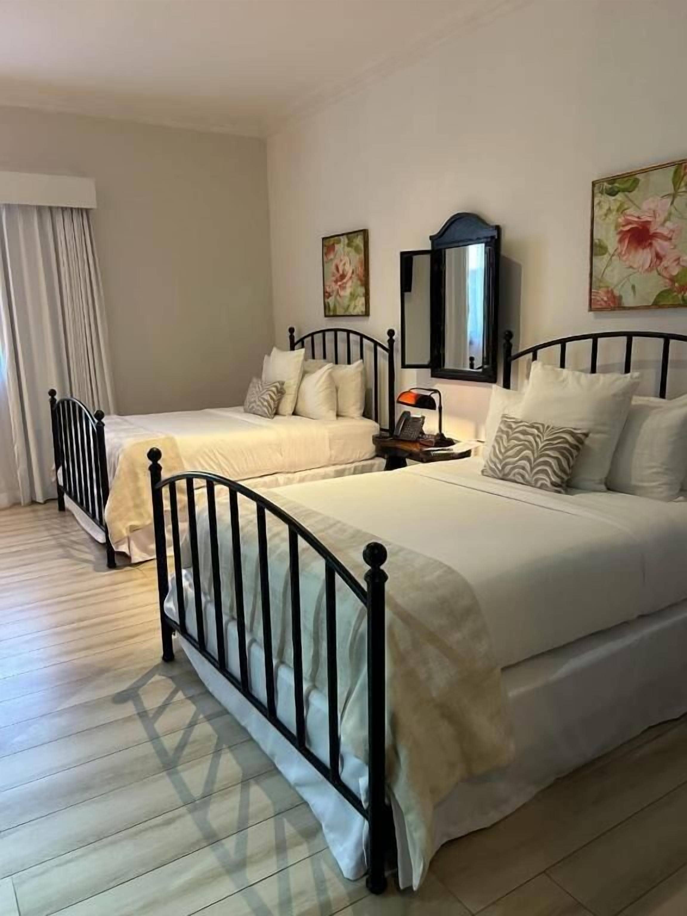 Une chambre double avec deux lits, une table de chevet avec une lampe et un miroir au mur.