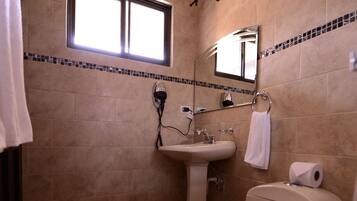 A bathroom with beige tiles, a sink, a toilet, a window, and a mirror.