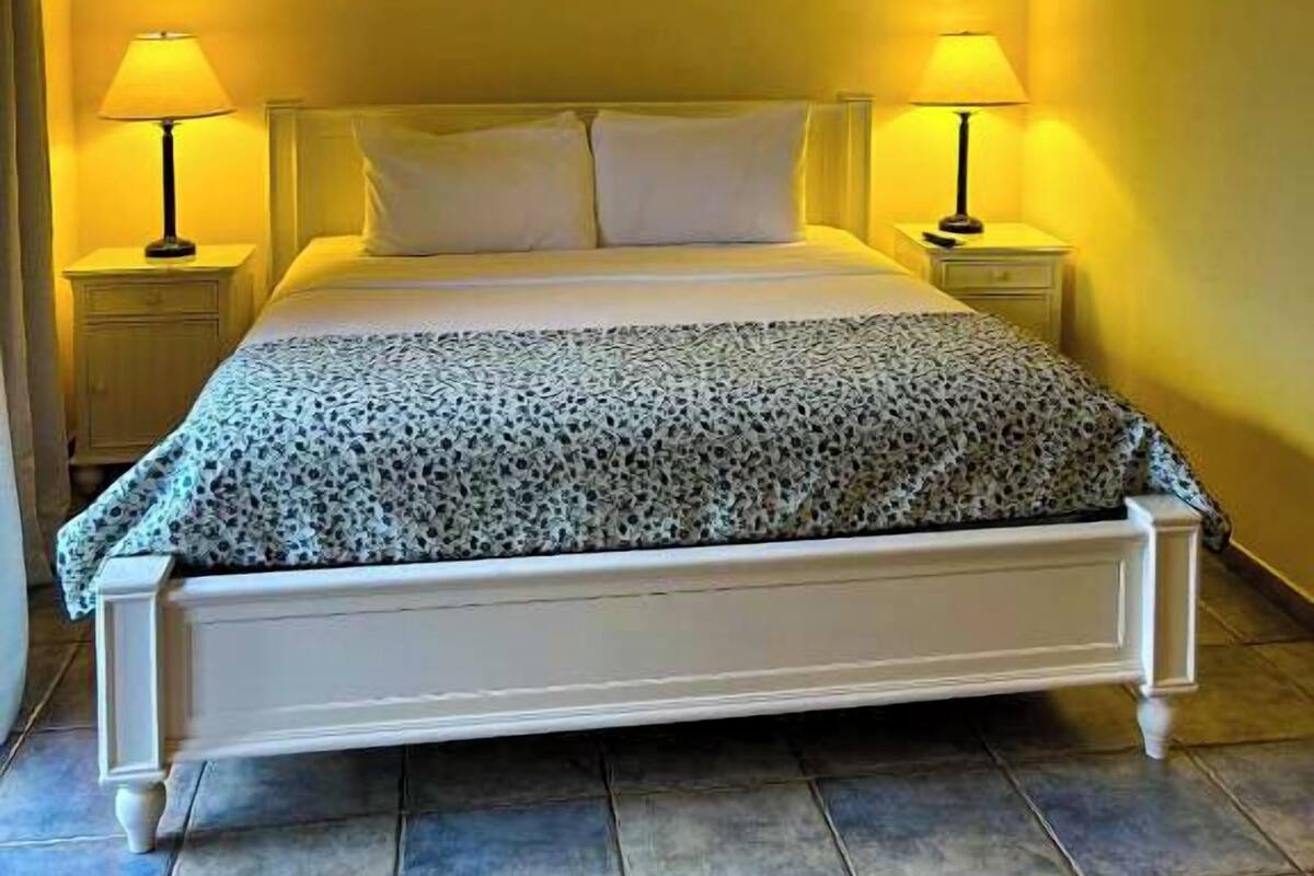 Una habitación de hotel con cama, dos lámparas de noche, ventilador de techo y ventana.