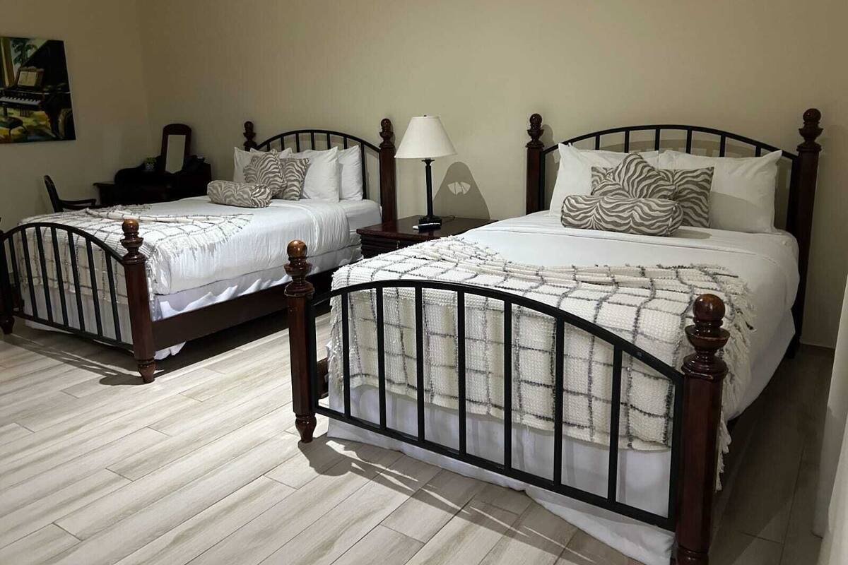 Dos camas de madera con estructura metálica, ropa de cama blanca y almohadas decorativas.