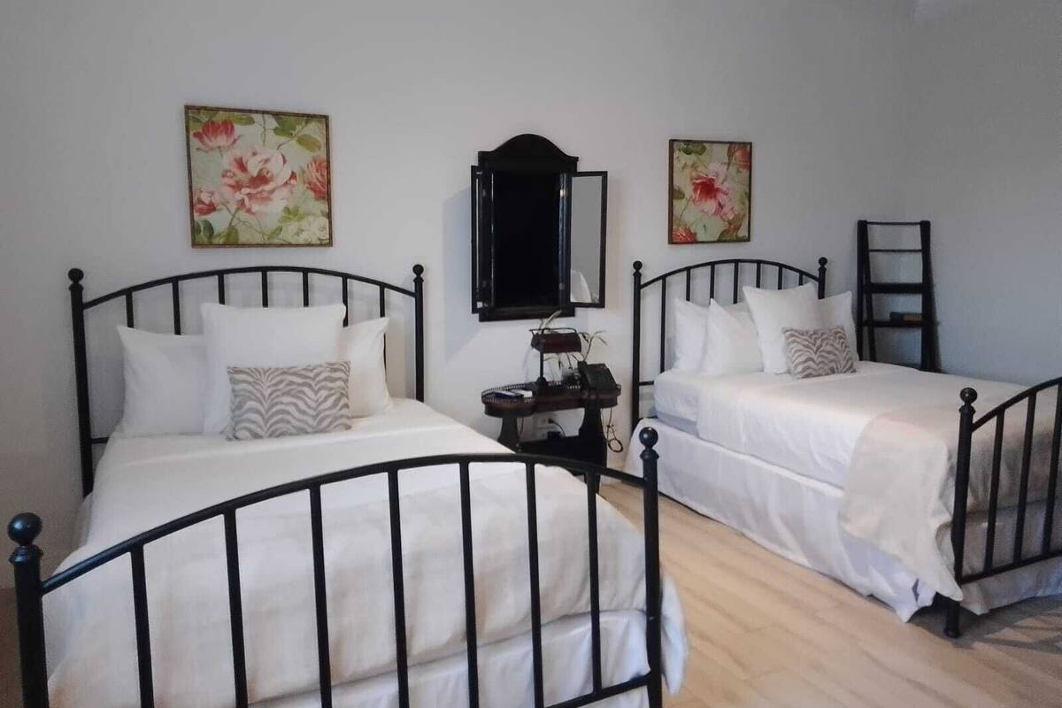 Una habitación con dos camas individuales, una mesita con un teléfono y dos cuadros con motivos florales en la pared.