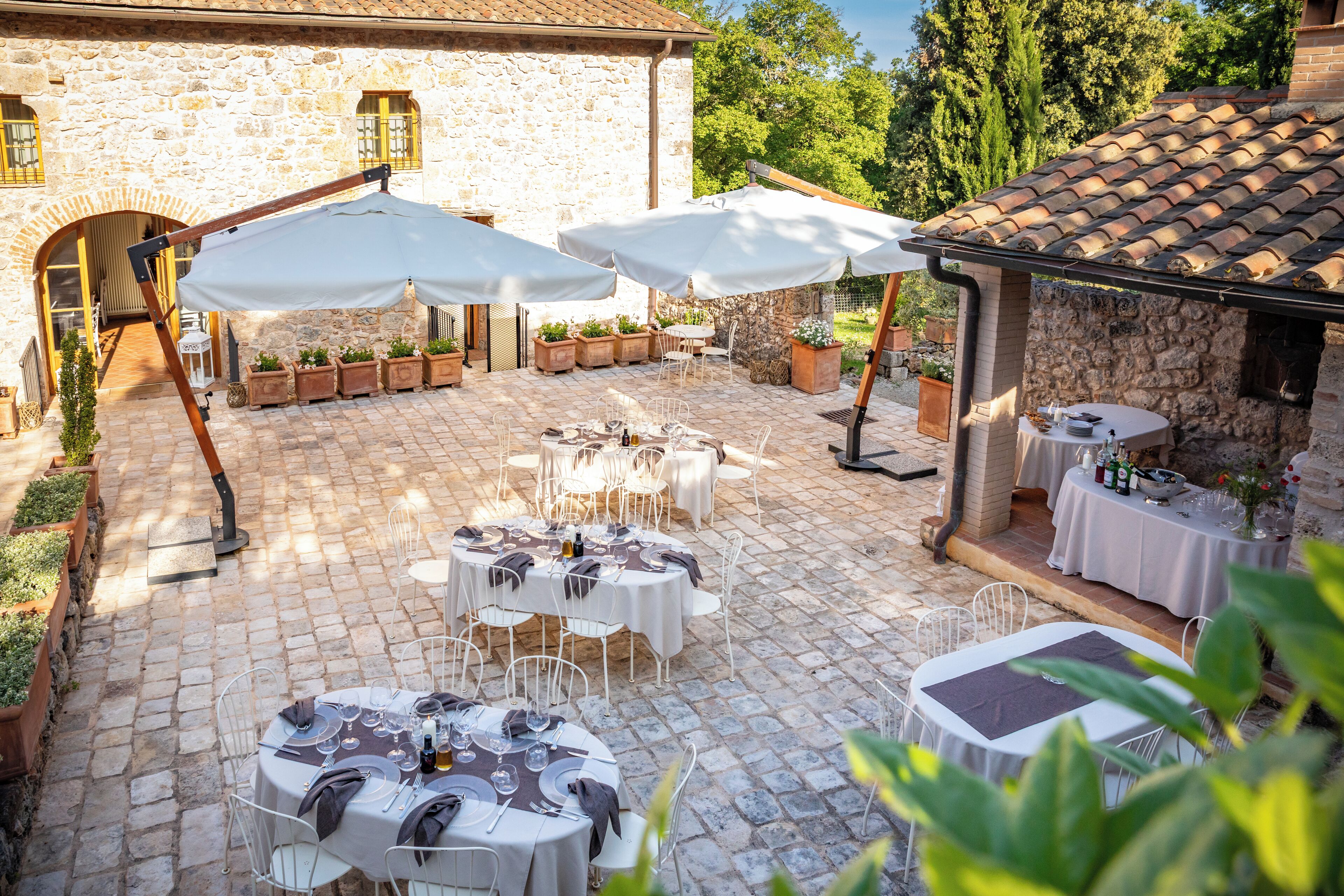 A courtyard with stone flooring, outdoor tables with white tablecloths, and umbrellas.
