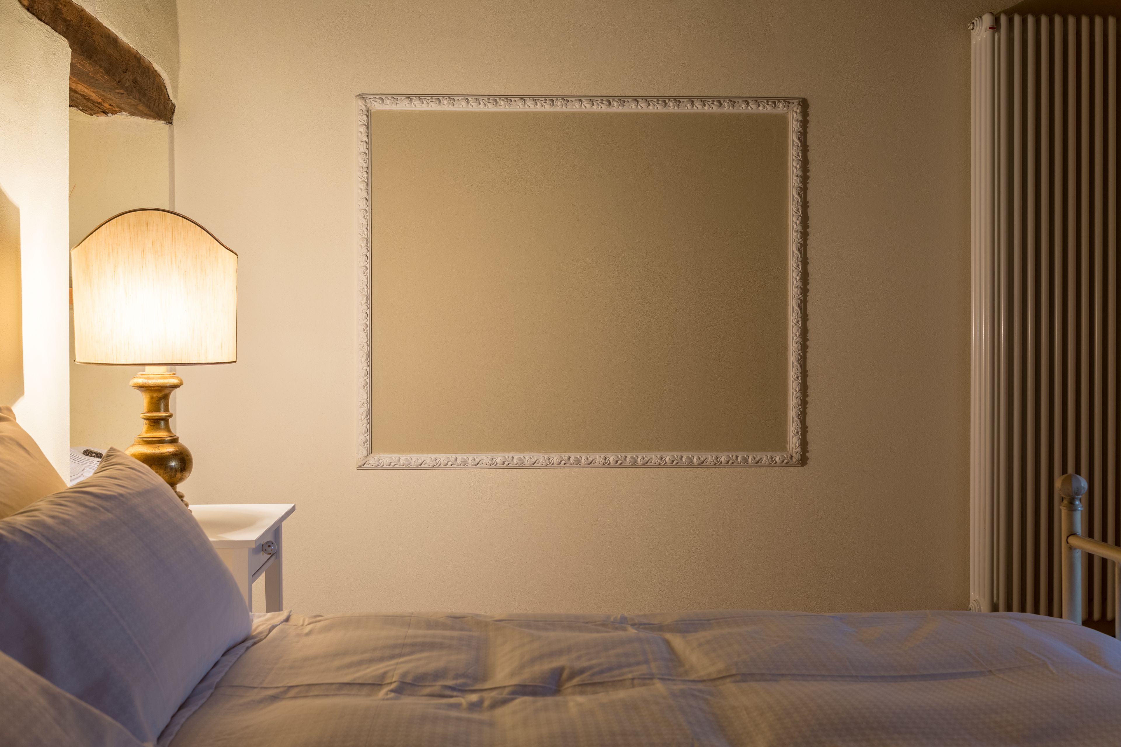 A bedroom with a bed, a nightstand, a lamp, and a wall-mounted mirror.
