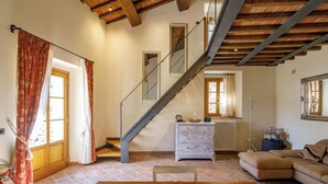Un salón amplio con escalera de madera, un sofá, una mesa de comedor y un radiador.