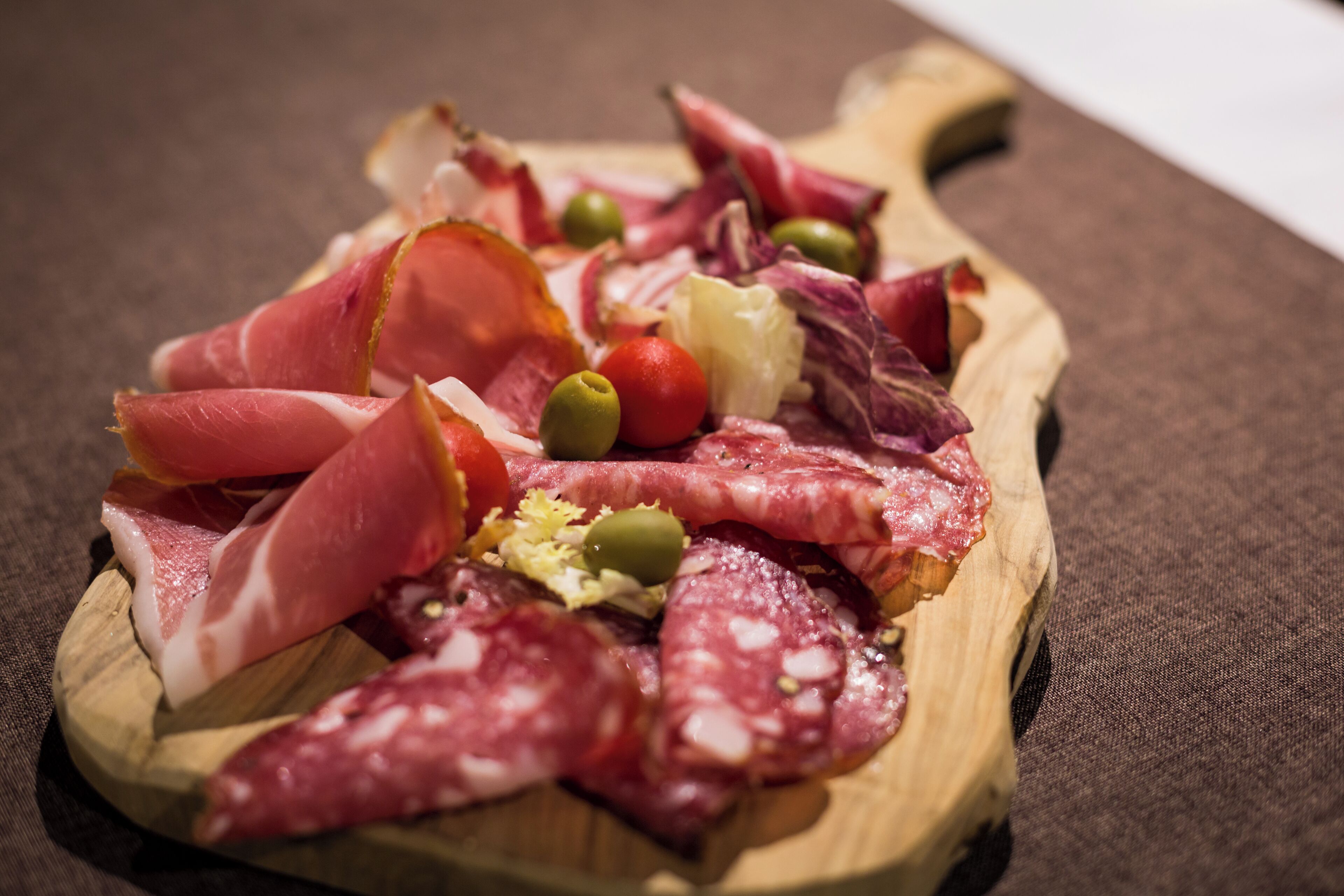 A wooden board with various cured meats and olives.