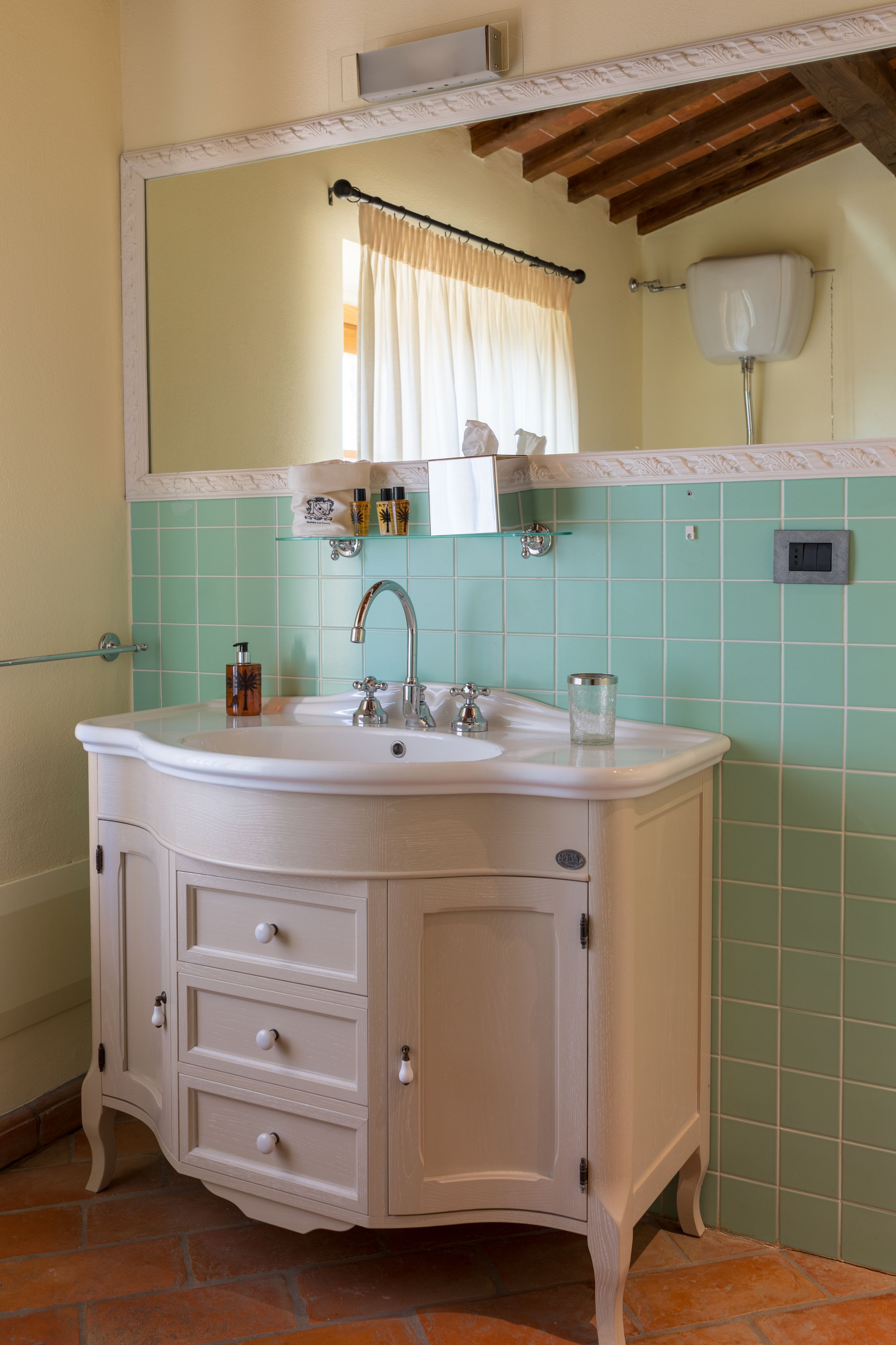A bathroom with a white vanity, a mirror, and a tiled wall.