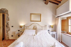 A bedroom with a bed, two bedside tables, a nightstand, a wall-mounted mirror, and a stone wall. - Relais la Costa - Dimora Storica (Monteriggioni)