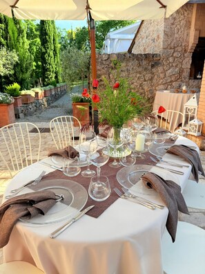An outdoor dining area with a stone wall backdrop, a table set with white tablecloths, clear glassware, and a vase with red flowers. - Relais la Costa - Dimora Storica (Monteriggioni)