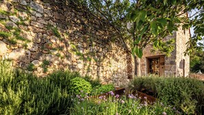 Un muro de piedra con un edificio rústico de piedra parcialmente visible detrás.