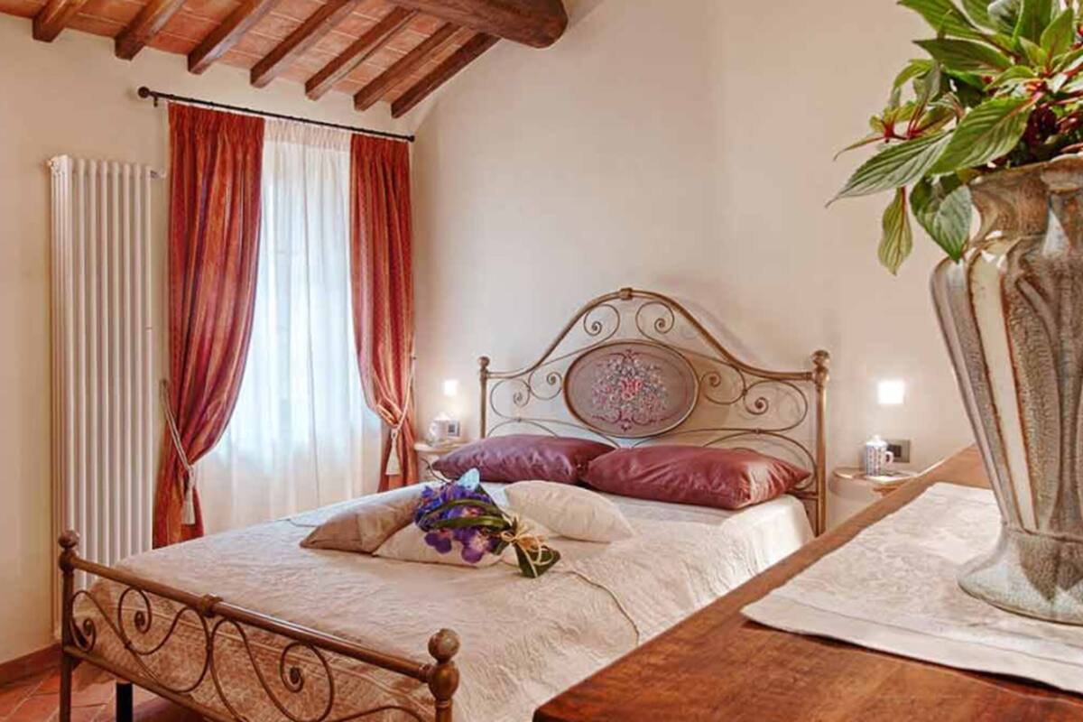 A bedroom with a bed, a nightstand, a vase with flowers, and a window with curtains.