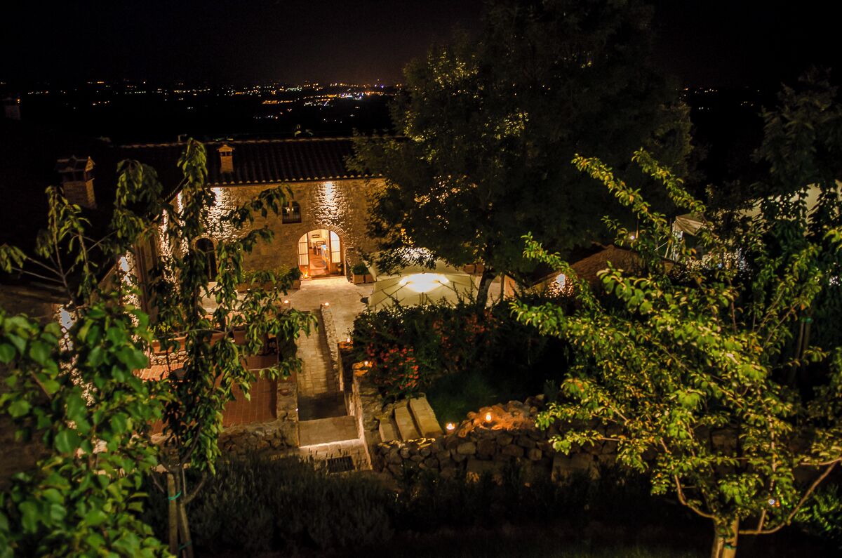 A nighttime view of a villa with a garden, a swimming pool, and a view of the city in the distance.