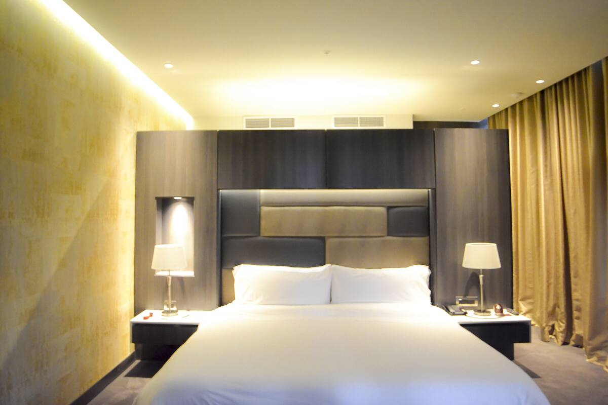 A hotel room with a large bed, two bedside tables with lamps, a headboard, and a curtain.