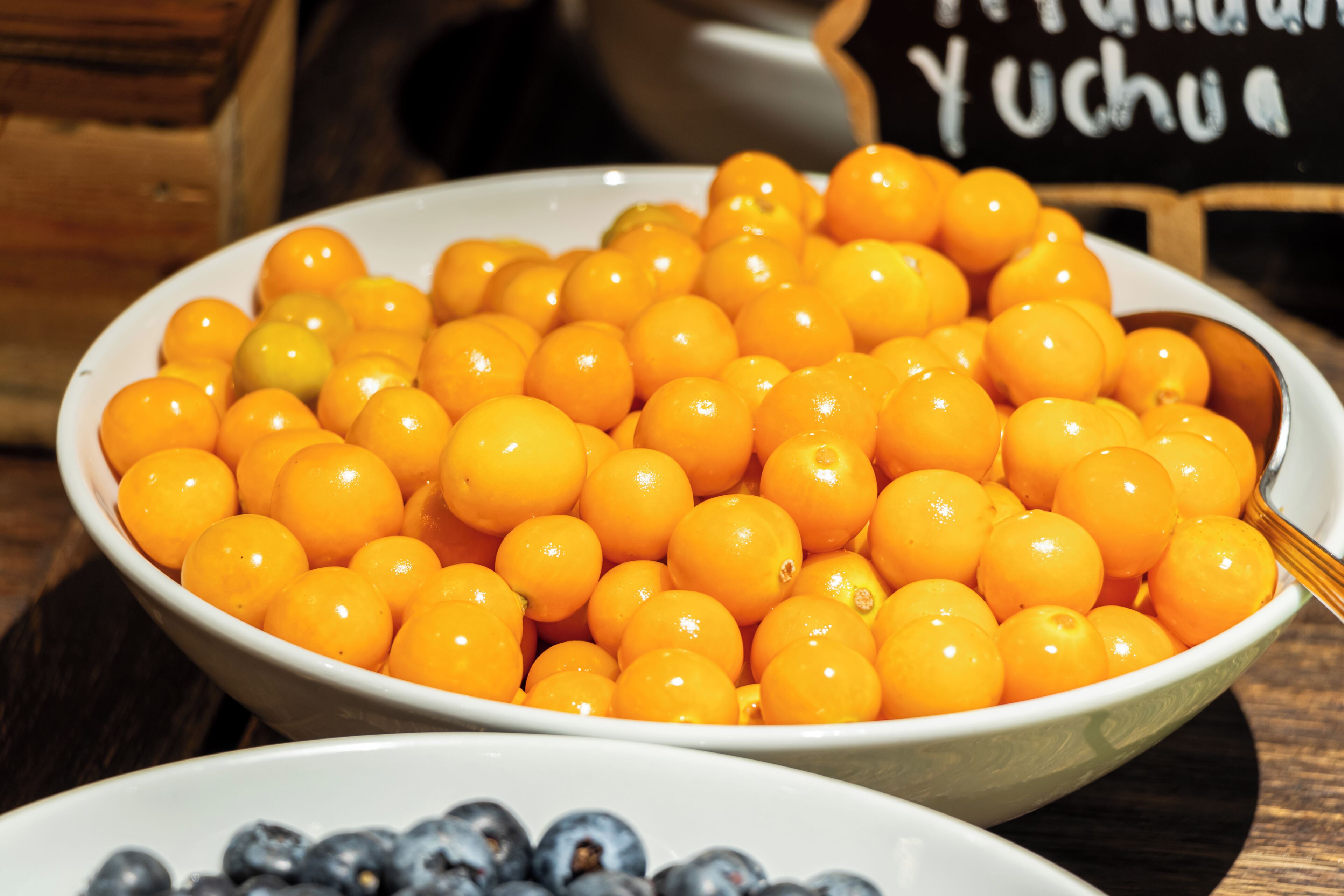 A bowl of bright orange fruits, likely yucchua, with a spoon in it.