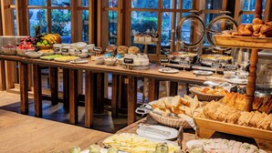 Un buffet proposant une variété de plats et de boissons, notamment des fruits, des fromages et des pâtisseries, présentés sur des tables en bois.