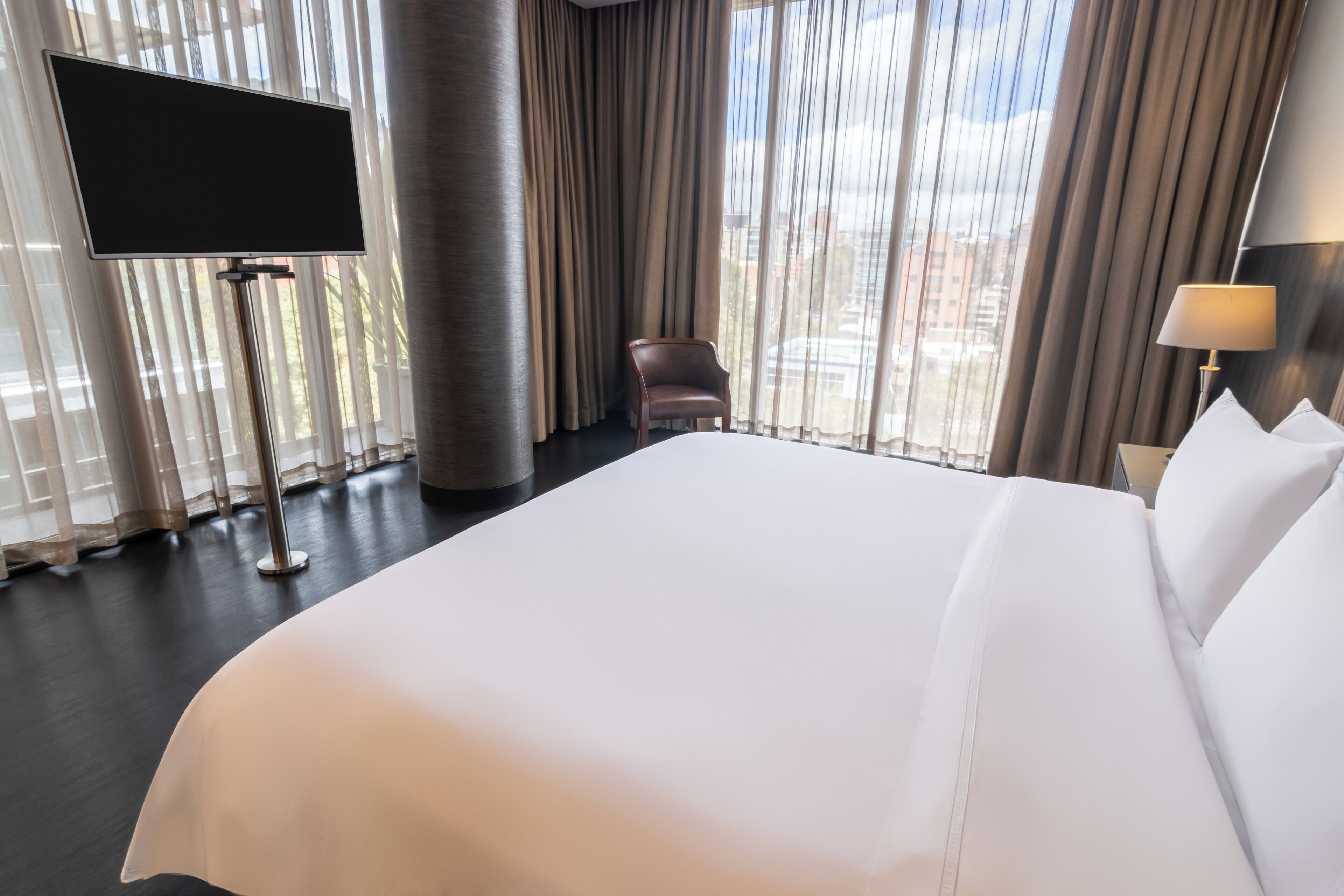 Una habitación de hotel con una cama grande, un televisor en un mueble, una silla y una lámpara.
