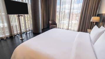 Una habitación de hotel con una cama grande, un televisor en un mueble, una silla y una lámpara.