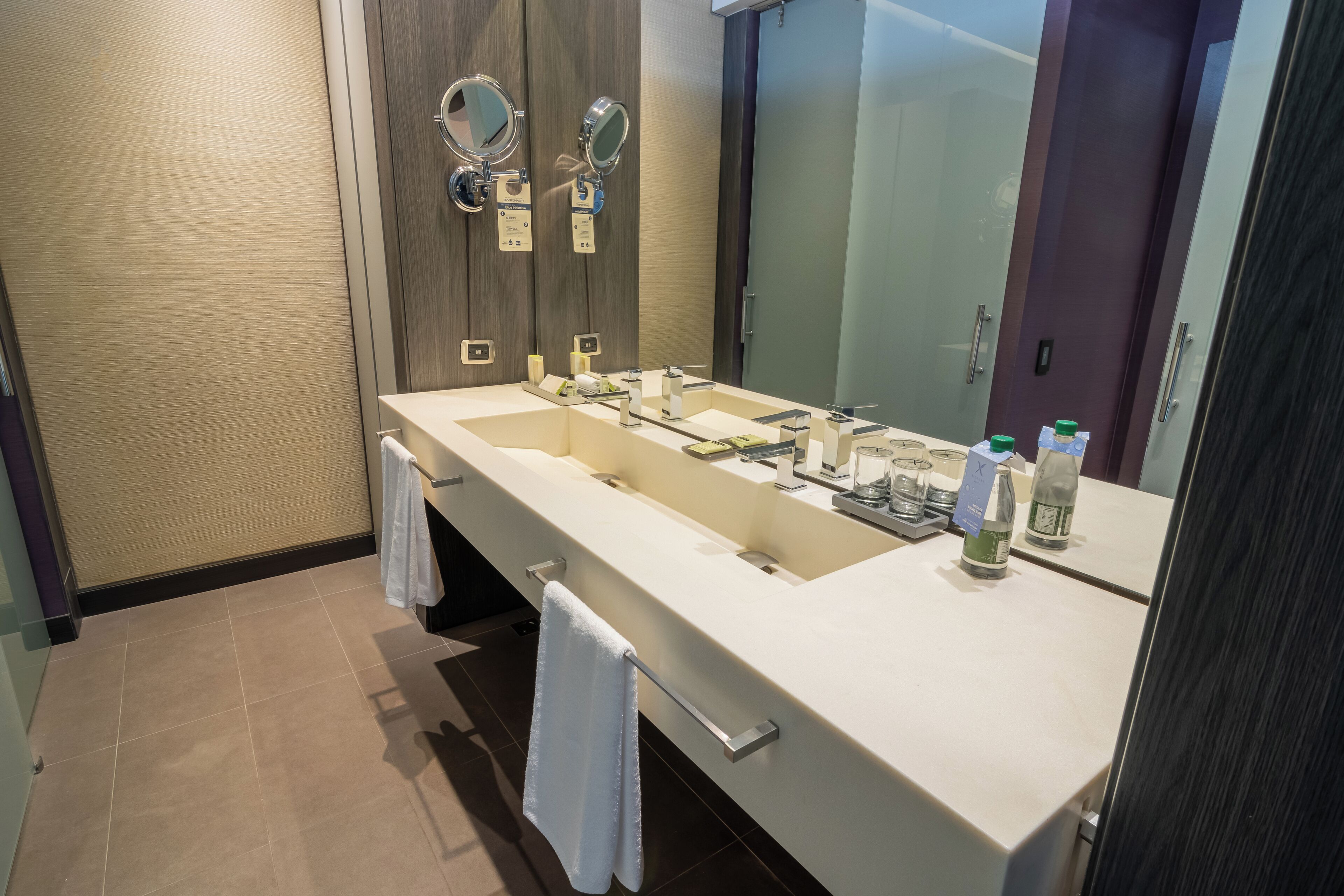 Un baño moderno con un lavamanos grande, dos espejos y un perchero para toallas.