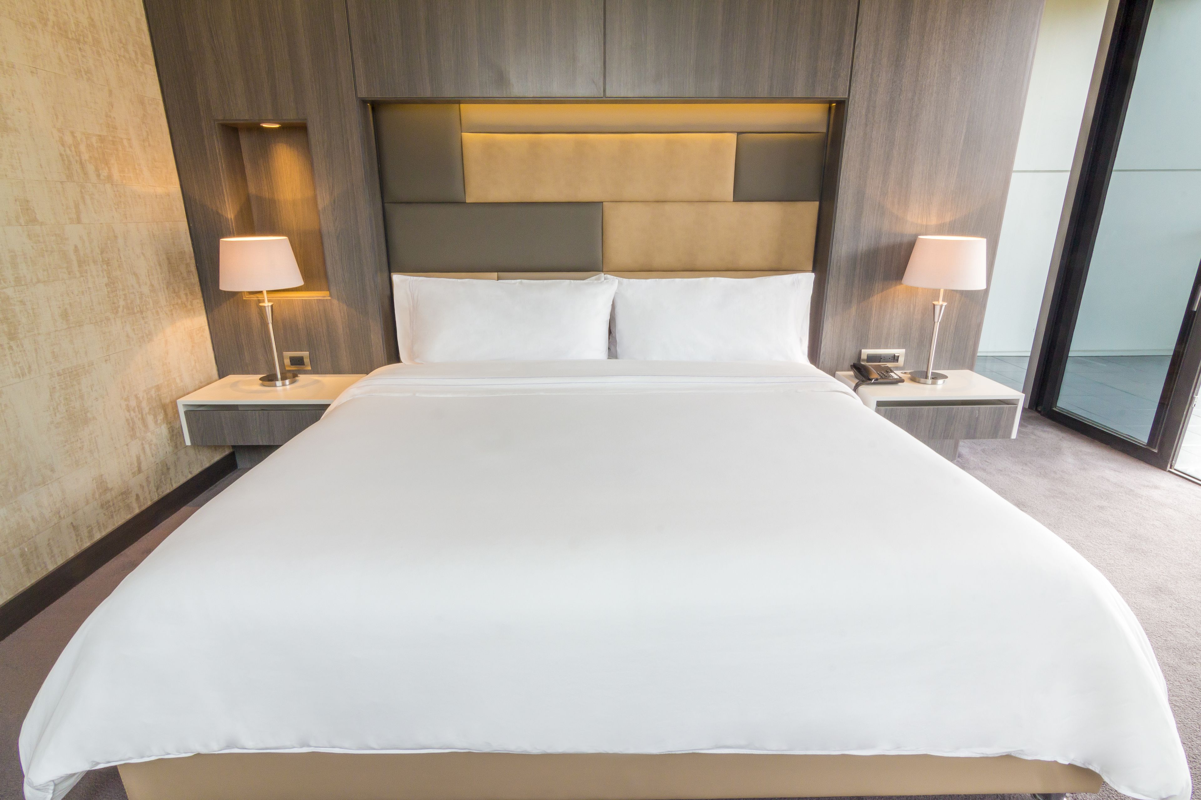 A hotel room with a large bed, two bedside tables with lamps, and a modern headboard.