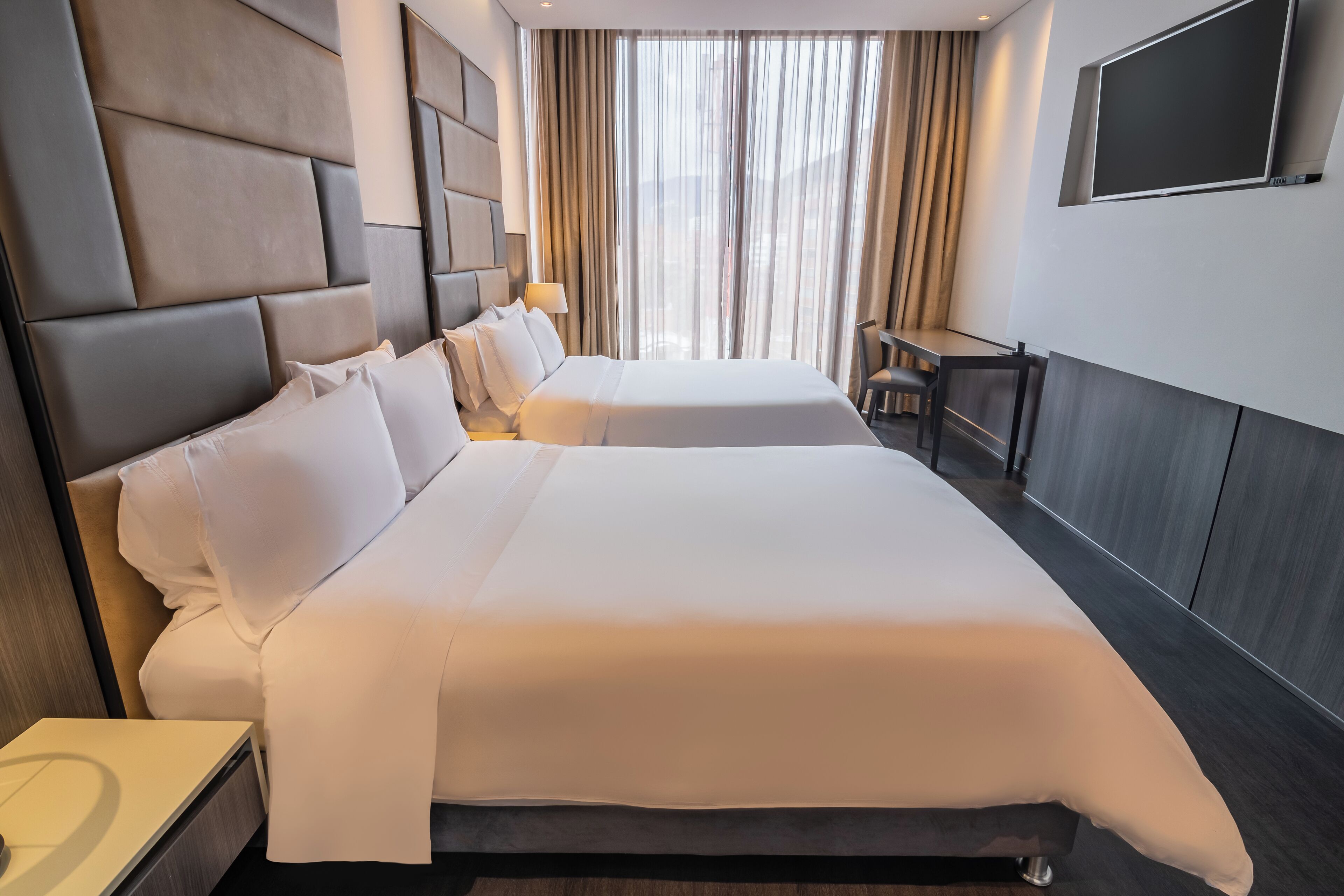 Ein Hotelzimmer mit zwei Betten, einem Schreibtisch und einem Fernseher.