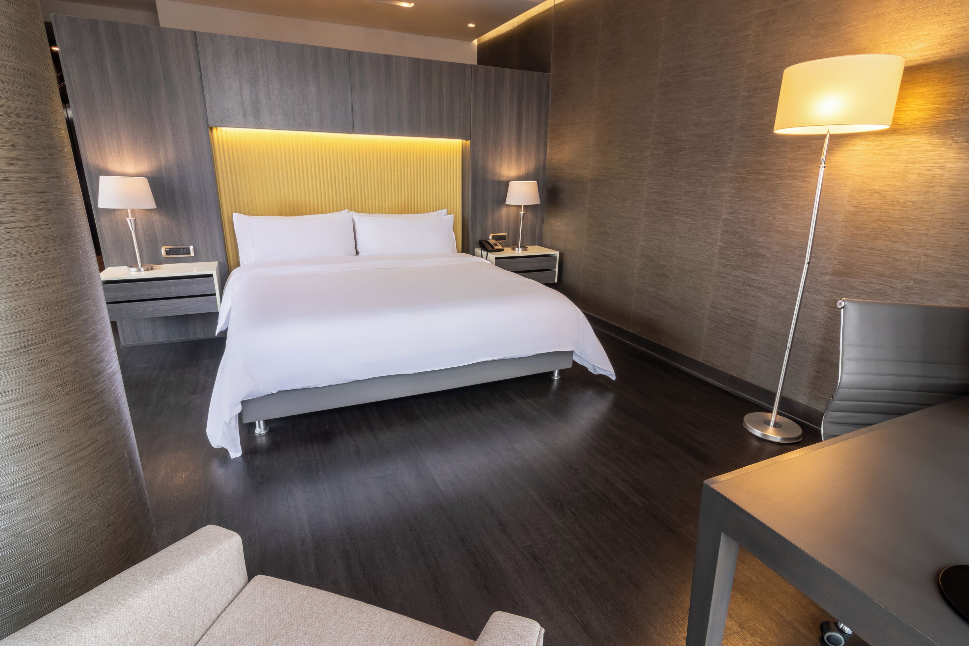 A modern hotel room with a large bed, two bedside tables with lamps, a desk, and a chair.