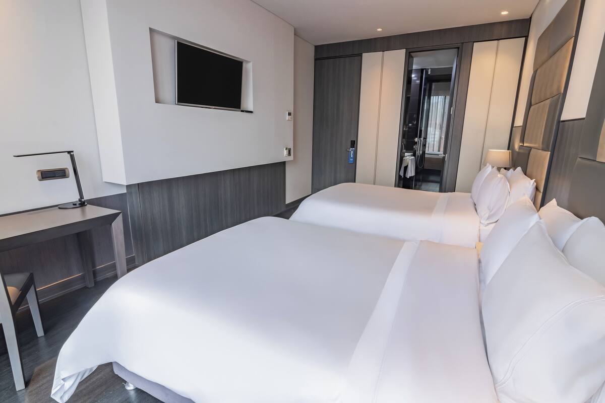 A modern hotel room with two beds, a desk, a TV, and a mirror.