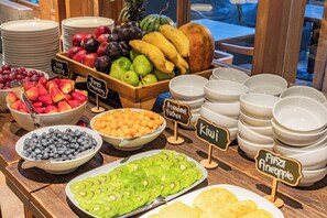 Een fruitschaal met verschillende soorten fruit en bakjes yoghurt.